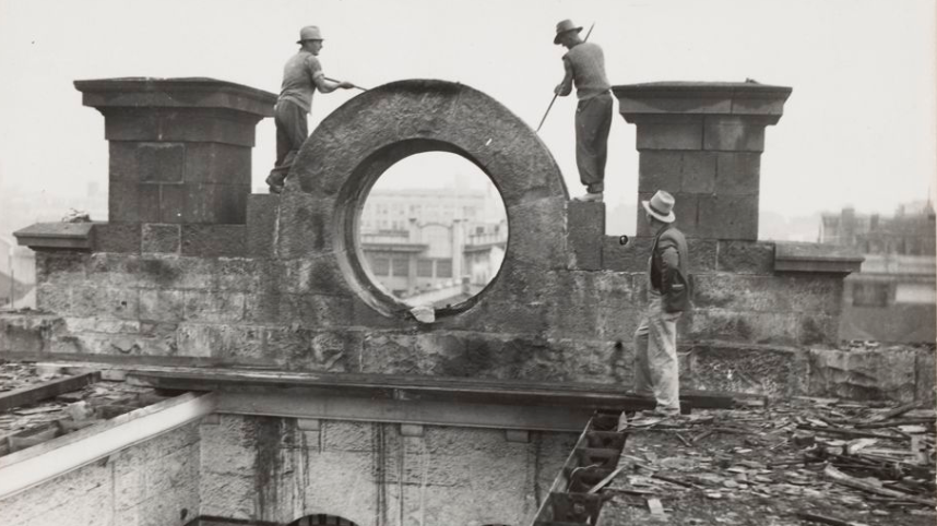 A historical black and white image of three workmen using tools to dismantle the Old Melbourne Gaol in the 1930s.