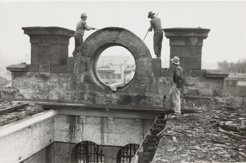 A historical black and white image of three workmen using tools to dismantle the Old Melbourne Gaol in the 1930s.