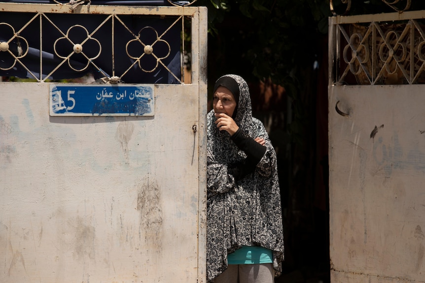 A woman in a head scarf peers out her doorway 
