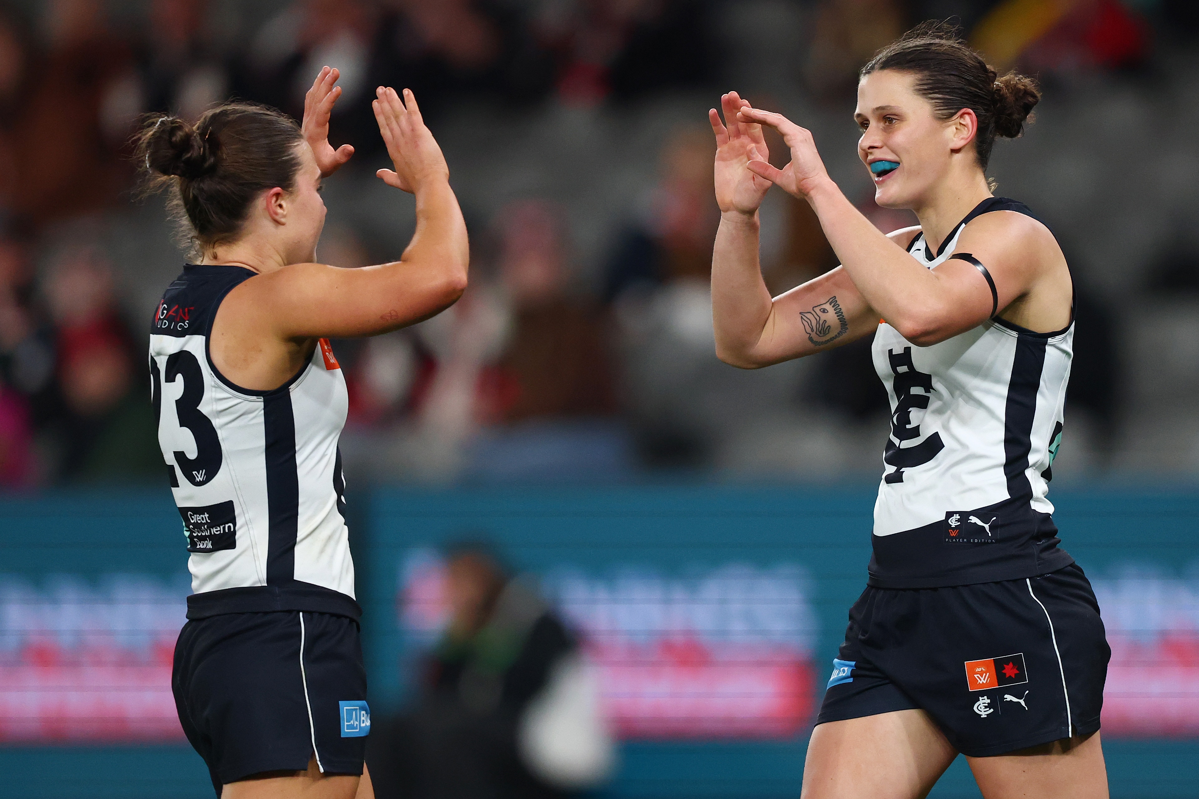 Two Carlton AFLW players clap hands in celebration after a goal by the player on the right.