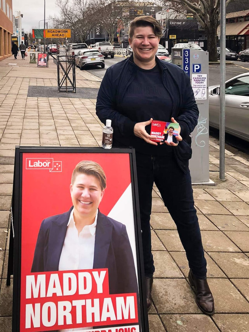 A smiling woman stands next to a campaign poster of herself.