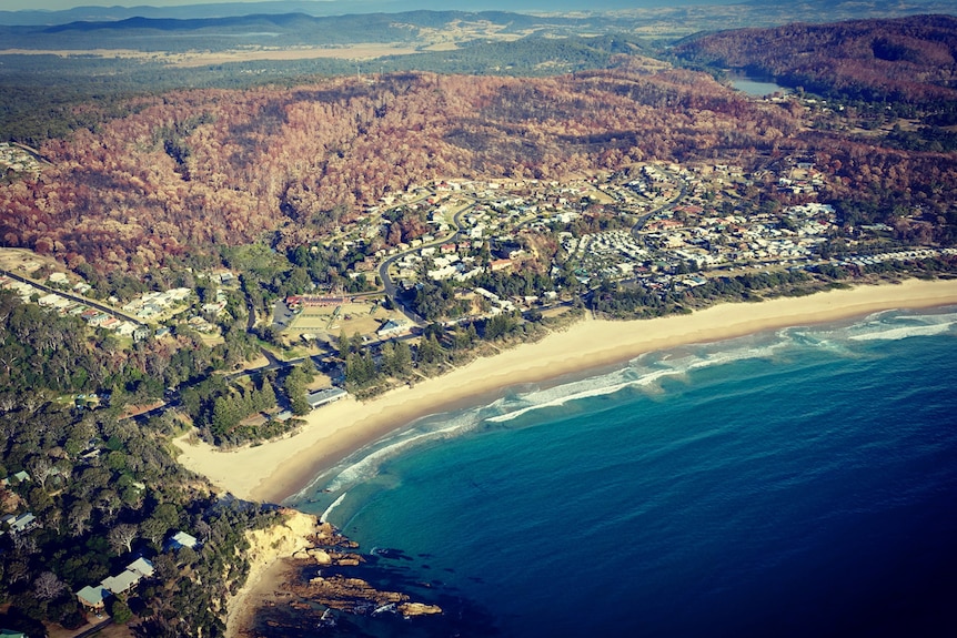 Aerial view of burnt bushland and houses in Tathra