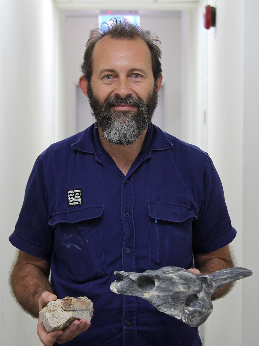 A photo of MAGNT's Jared Archibald holding a piece of limestone and a replica skull.