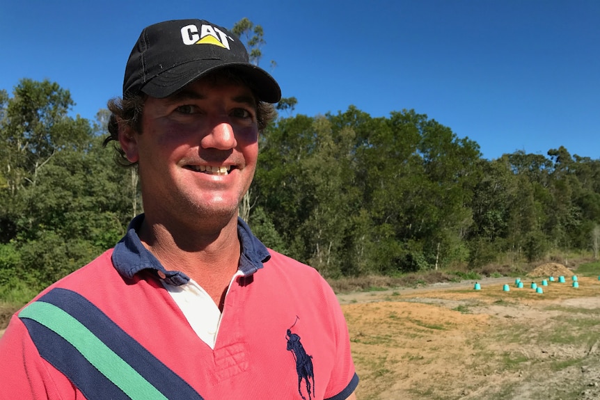 A man with curly hair, a red shirt and a cap standing in front of the upturned buckets.