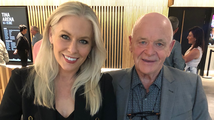 Smiling woman with blonde hair, with bald man in grey jacket