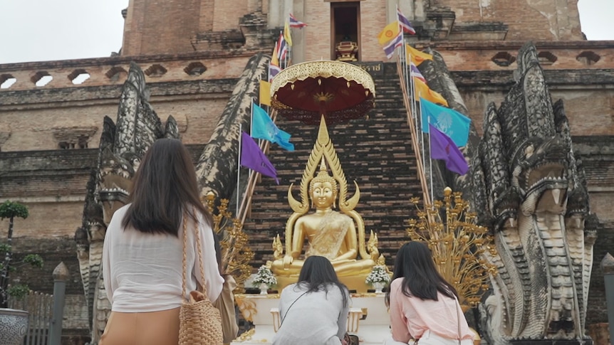 Three people kneel on the ground in front of a gold statue.
