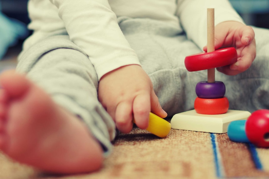 Close up of toddlers hands playing with small, colourful abacus