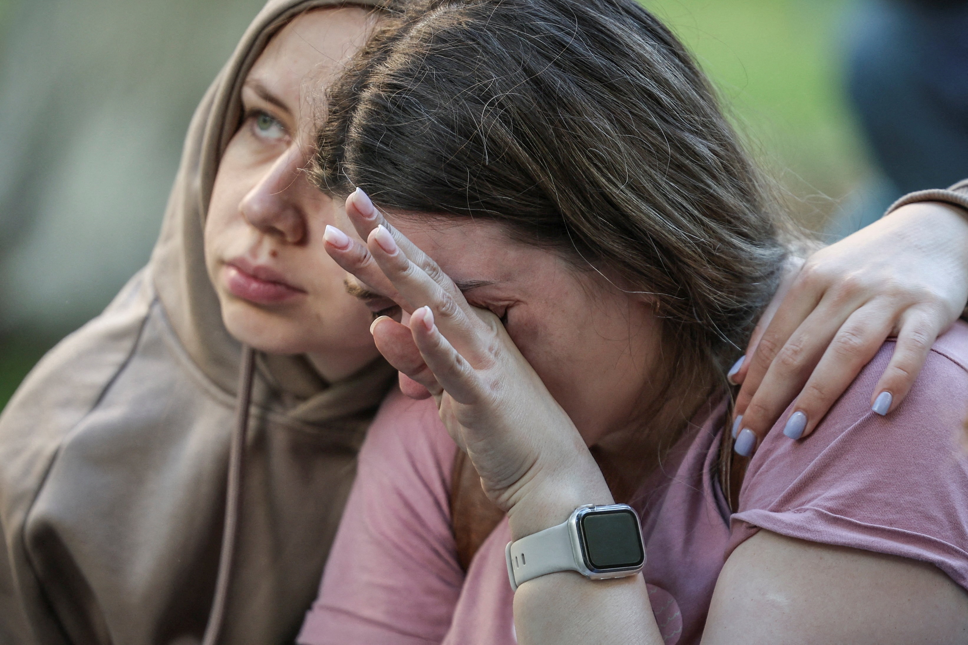 A girl in a hoodiw puts her arm around another young girl who is crying. 