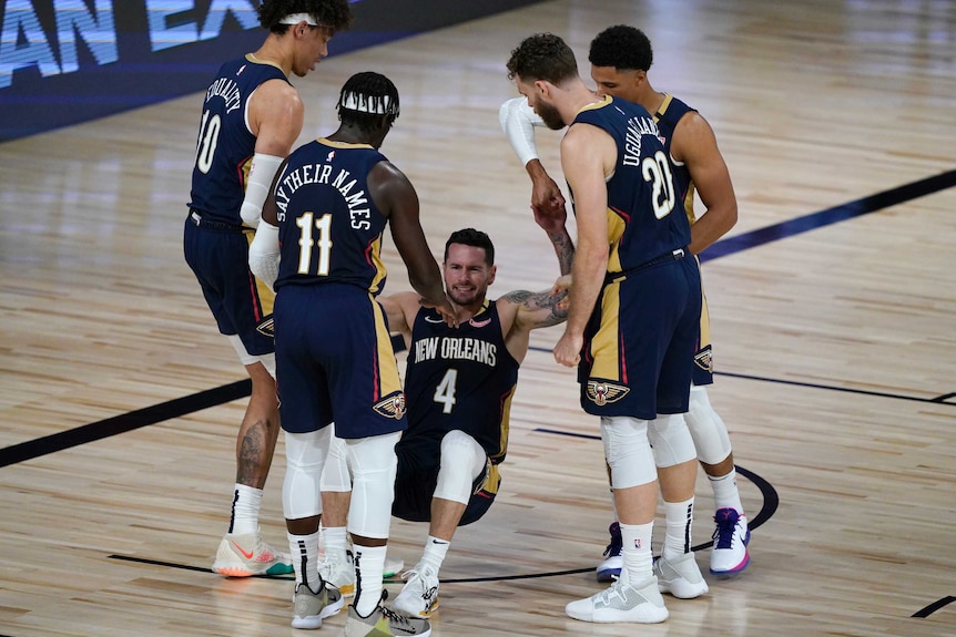 Four Pelicans players surround one to help him off the floor. One player has "SAY HER NAME" on the back of his jersey