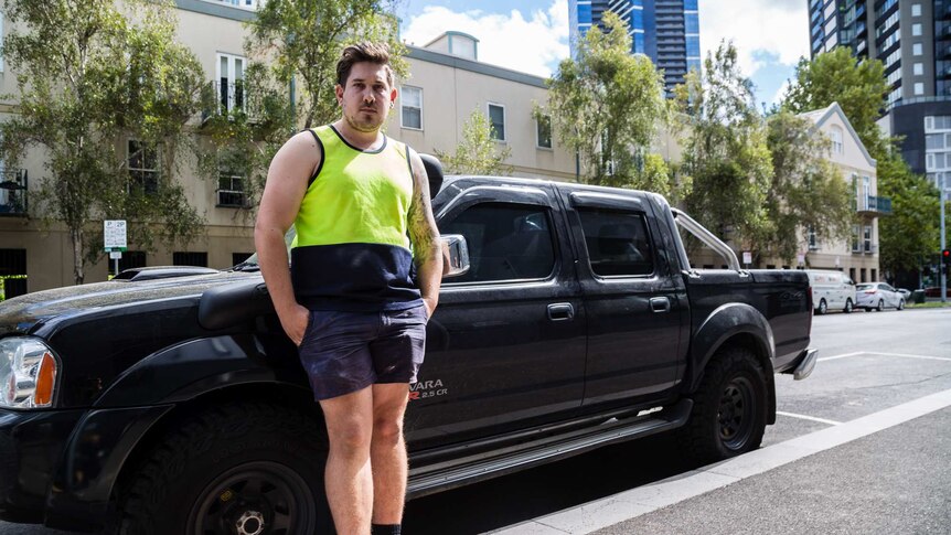 Dressed in a high-visibility singlet and shorts, Alex stands in front of a ute.