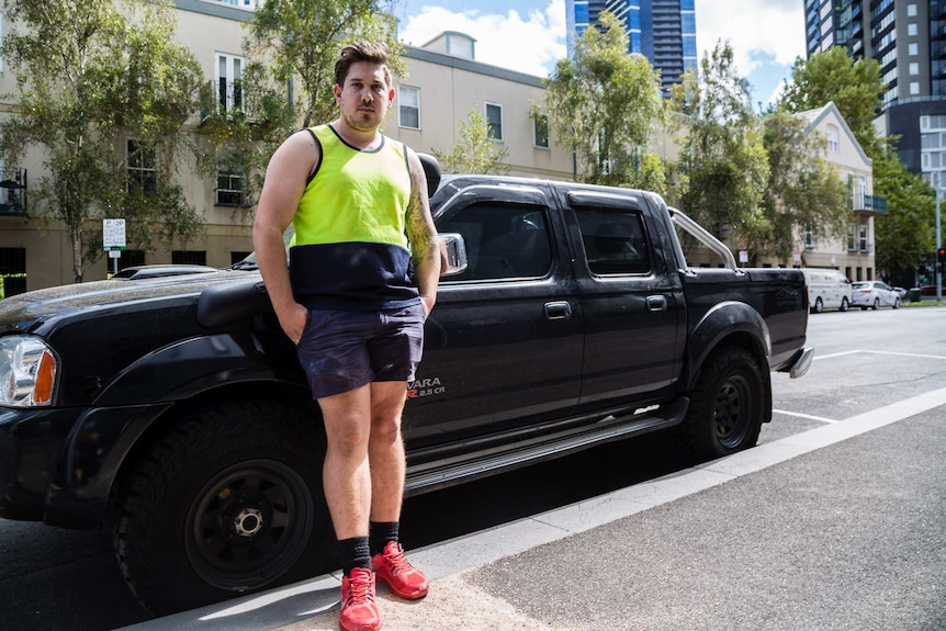 Dressed in a high-visibility singlet and shorts, Alex stands in front of a ute.