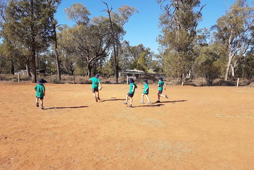 Children playing soccer on a bare playground at school.