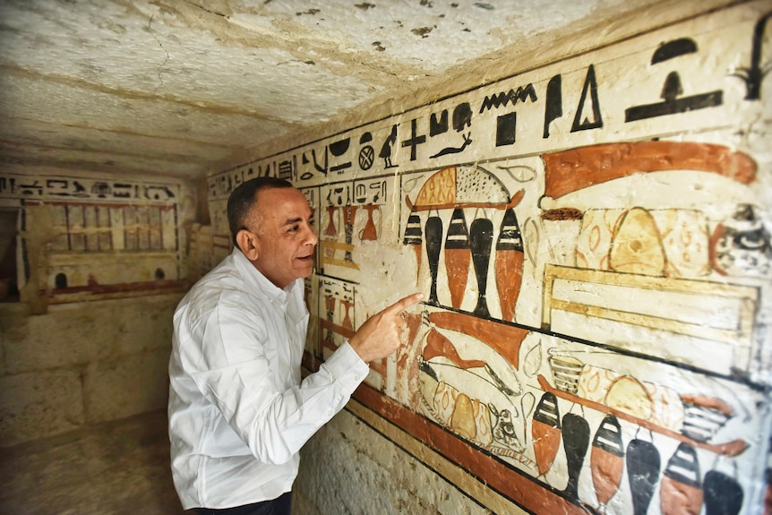 Man stands next to ancient wall paintings 