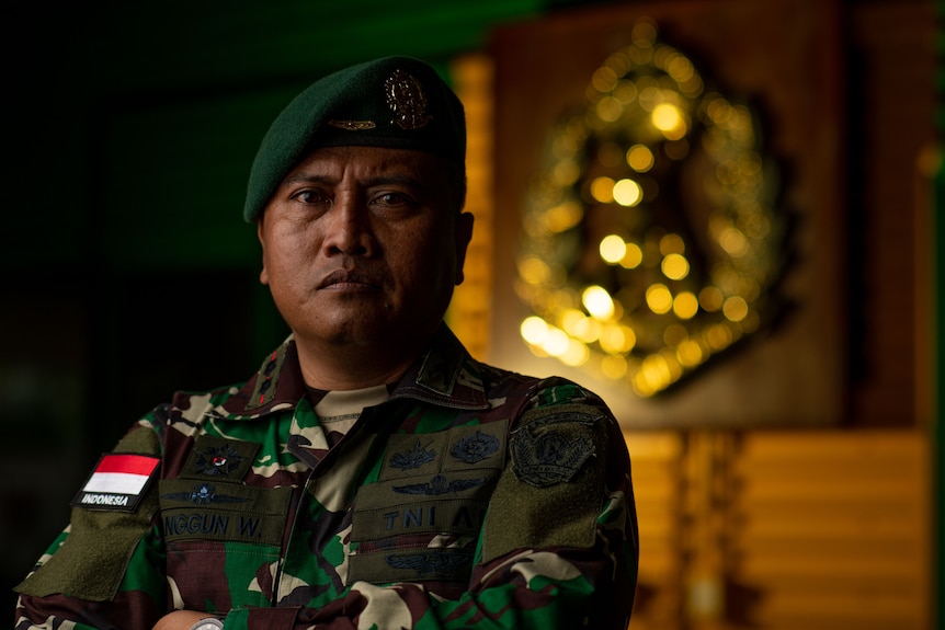 Un soldat indonésien vêtu d'un chapeau mou et d'un camouflage, les bras croisés, l'air sévère.