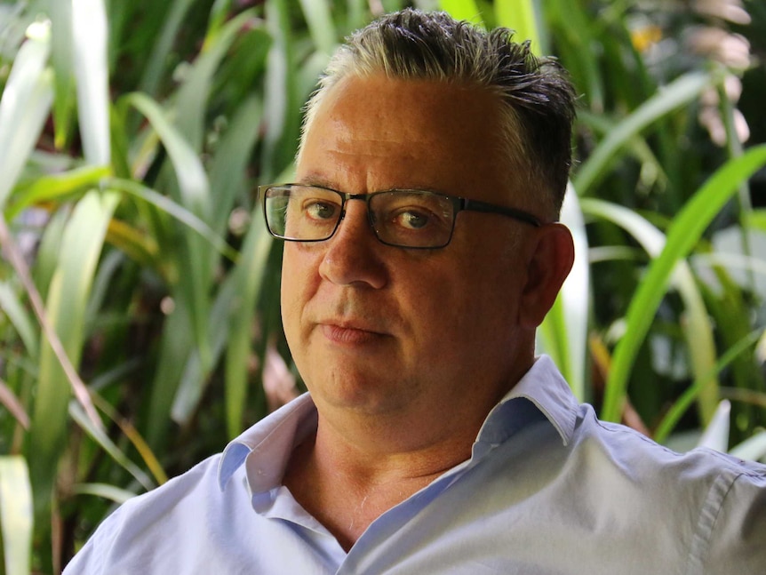 Headshot of a man in glasses against a plant backdrop.