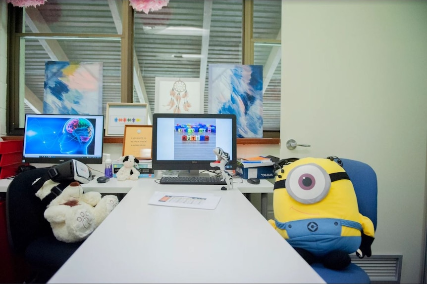 A desk with computer monitors and a stuffed toy sitting on a seat