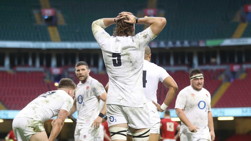 An England player holds both his hands on top of his head as seen from behind as other players look towards him