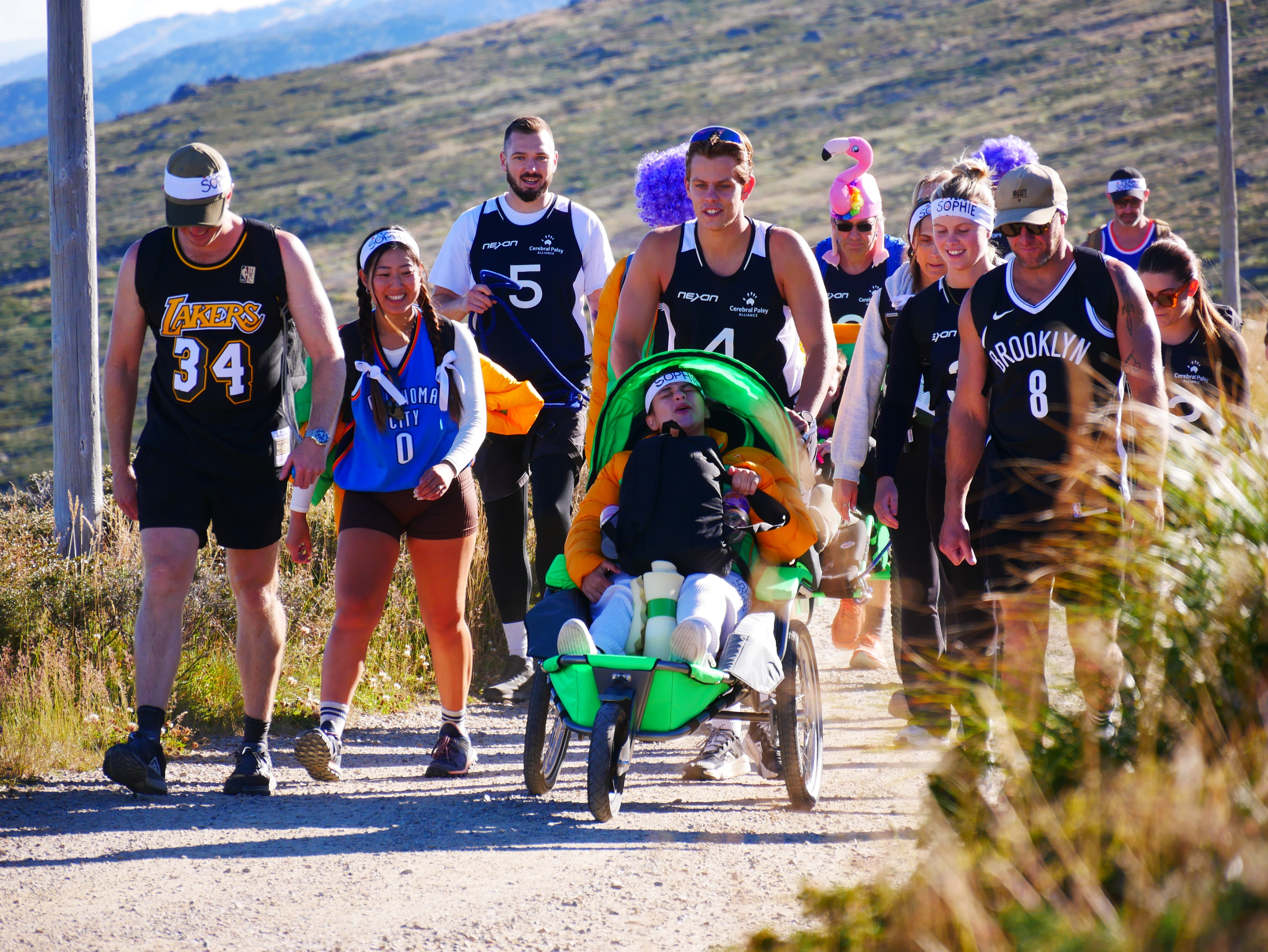 a group of people walk uphill and push a man in a wheelchair.