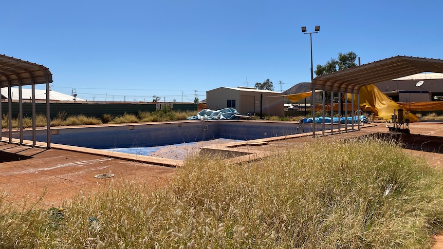 Empty public pool in remote community, orange dirt, grass in the foreground.