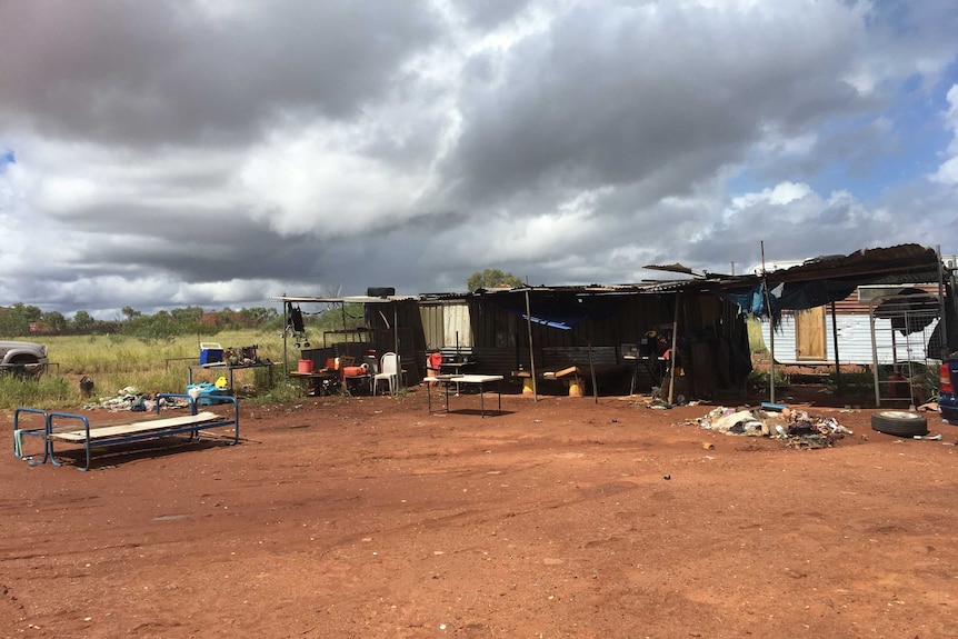 A dilapidated tin shed and bed outdoors in a town camp.