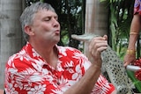 Ron Kelly in a floral t-shirt kissing a crocodile.