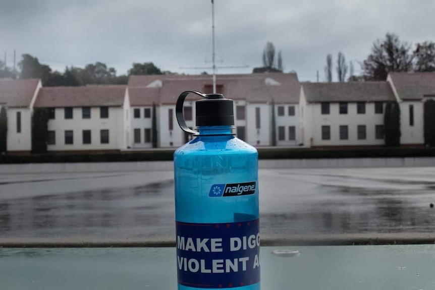 A water bottle with a sticker that reads Make Diggers Violent Again with Duntroon military college in background