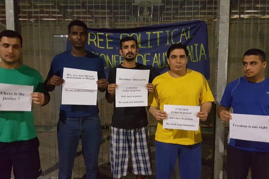 A line of five refugees holding up signs protesting for their freedom and justice.