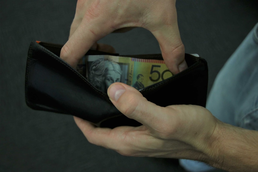 Someone reaches into their wallet to get a $50 note