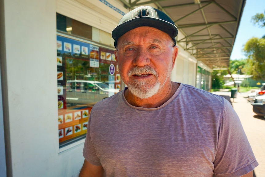 Man in cap stands outside shop and smiles at camera