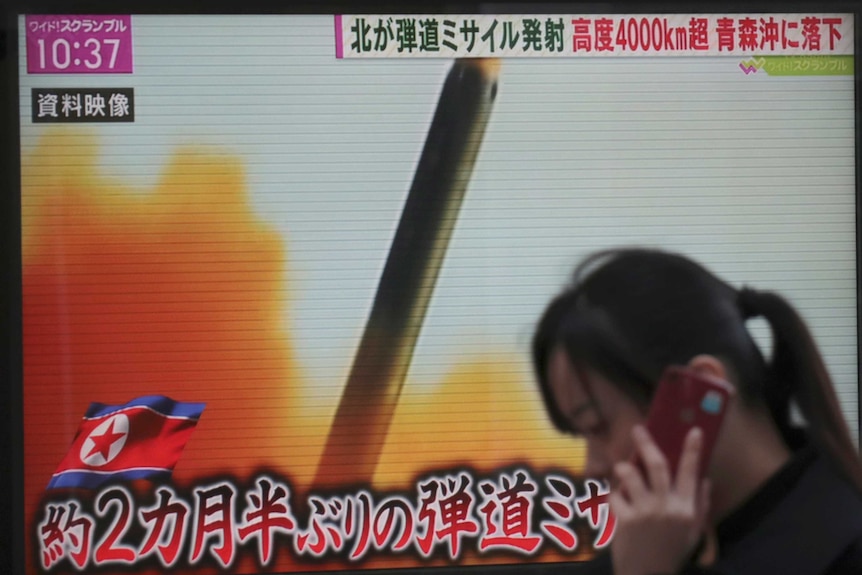 A woman walks past a TV screen broadcasting news of North Korea's missile launch
