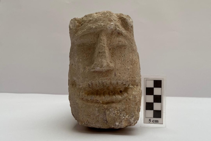 A sculpture of a stylised, elongated head sits next to a marker that displays measurements in centimetres.