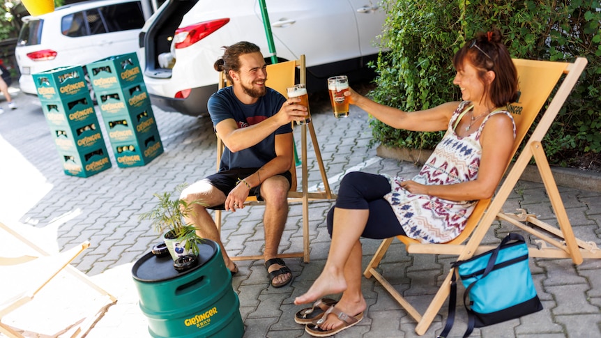 A man and a woman sitting and toasting with a glass of beer in their hand.
