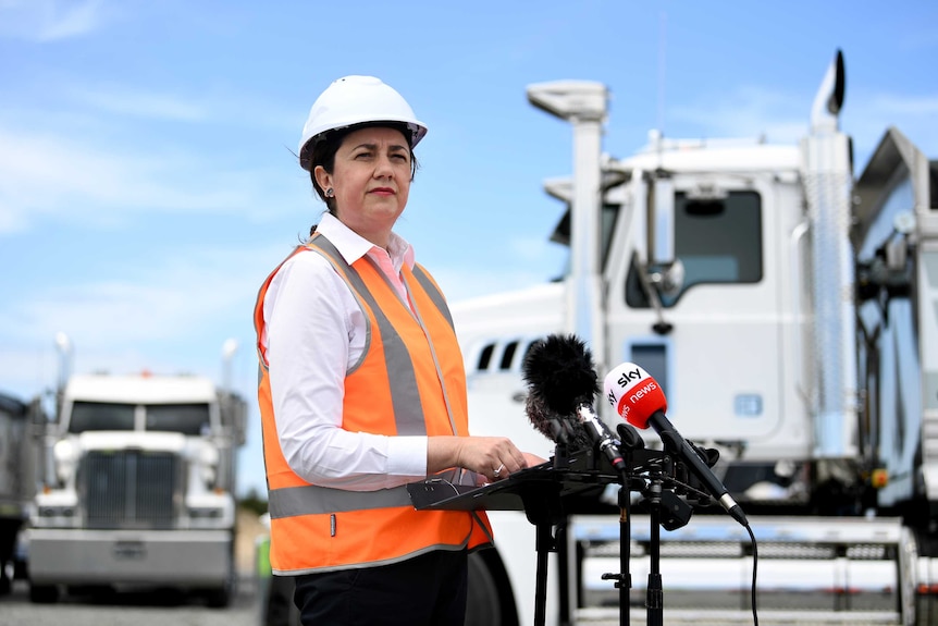 Queensland Premier Annastacia Palaszczuk looks on during a press conference and wearing hard hat and high viz vest