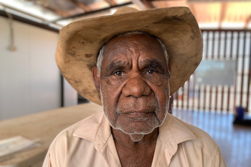 Indigenous male elder with country hat has neutral look on his face