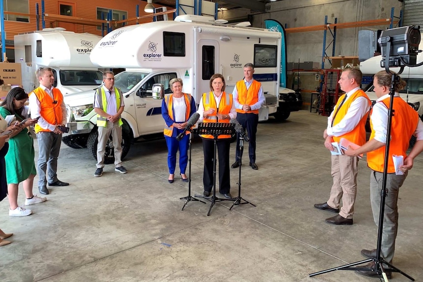 Politician in high-vis vest answers questions at a press conference.