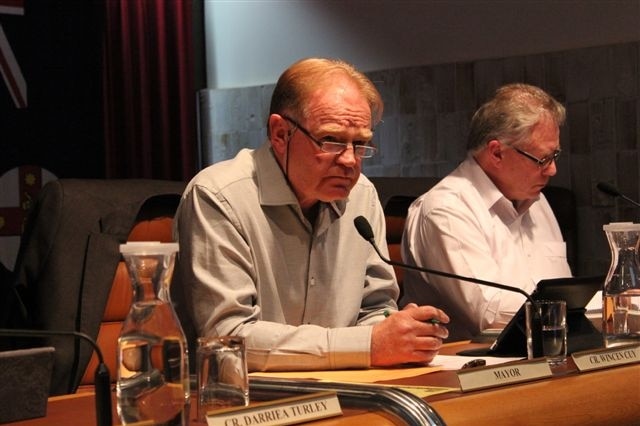 A man speaks into a microphone while sitting at a desk.