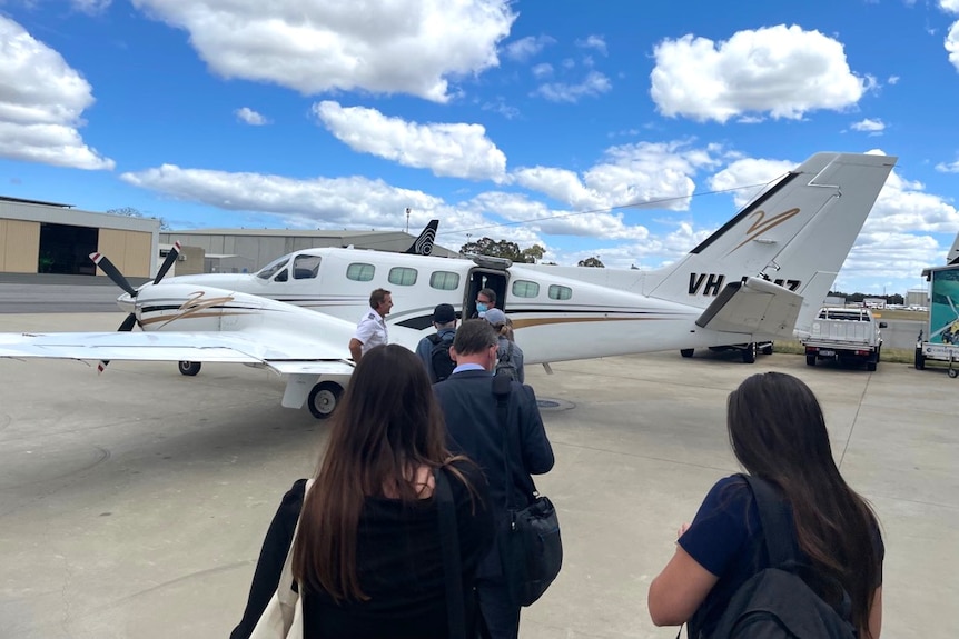 A stream of people walk across a tarmac towards a small charter propeller plane.