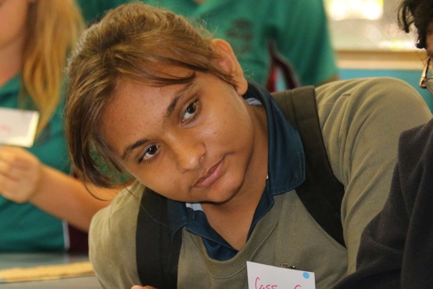 A girl sitting at a table with other students participates in a workshop.