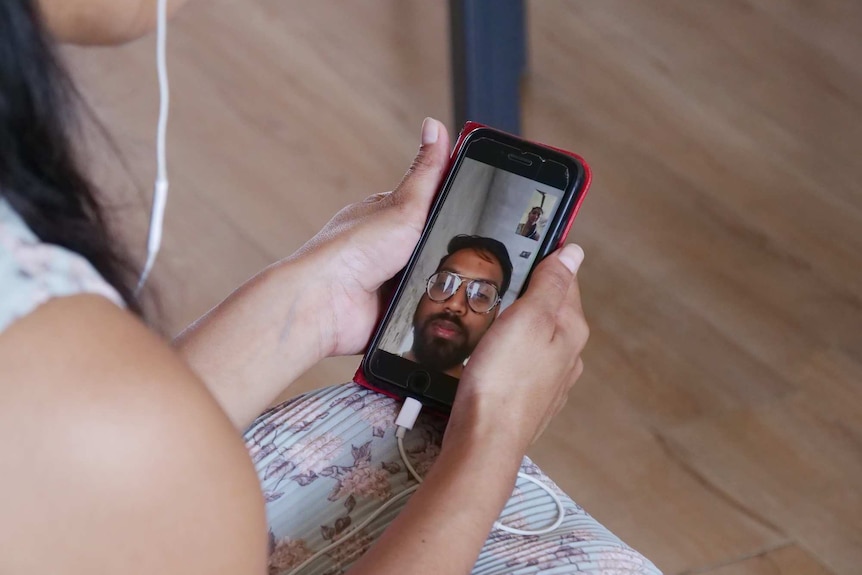 Asma Mukhi's hands hold a mobile phone during a video call, with her husband seen on the screen.