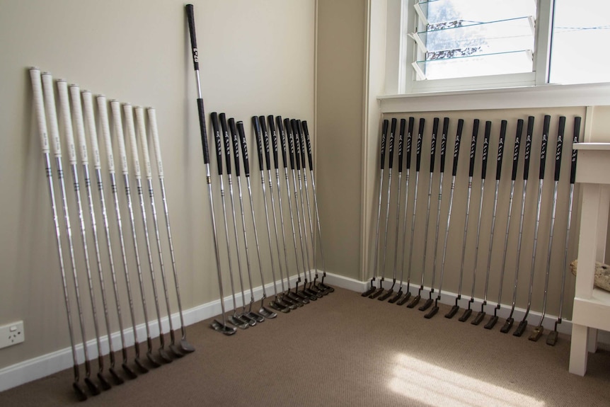 Golf putters lined up against a wall.