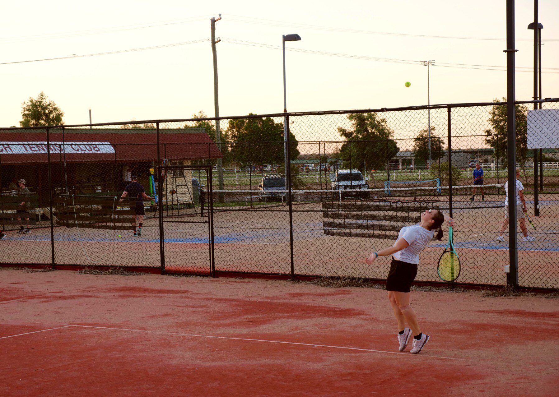 Woman serving on red tennis court.