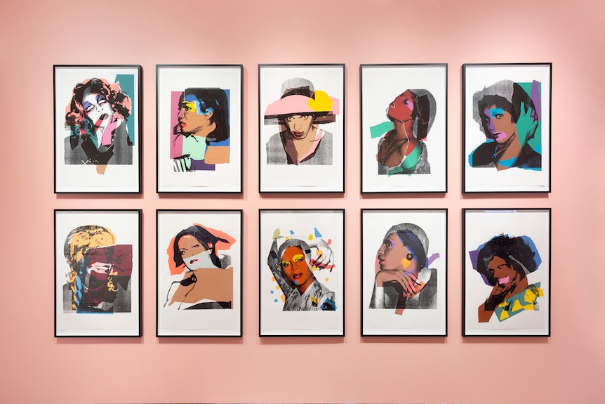 10 pop art graphic portraits hung in two rows of five in front of a salmon coloured wall