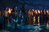 A male and a pregnant female Na'vi stand in water surrounded by other Na'vi holding torches