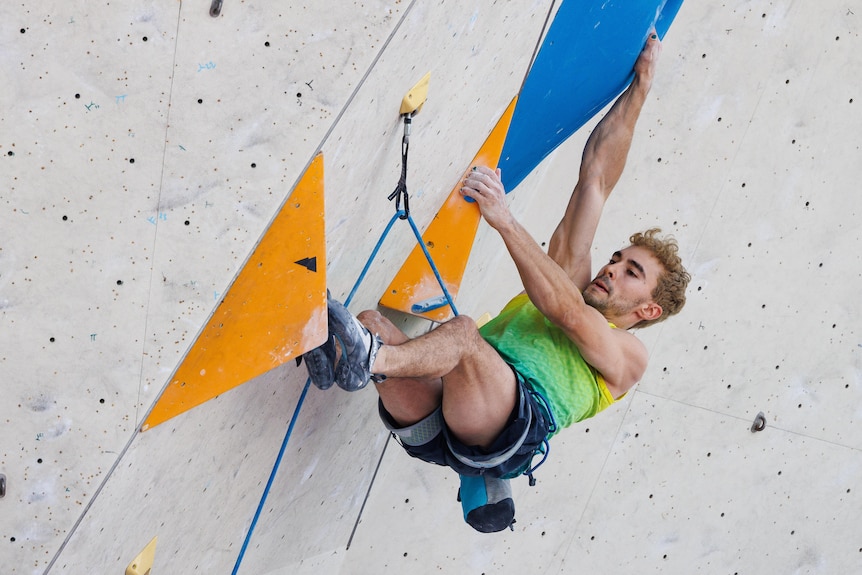 Sport climber Campbell Harrison has his legs and arms outstretched on boulders while scaling an indoor rock climbing wall.