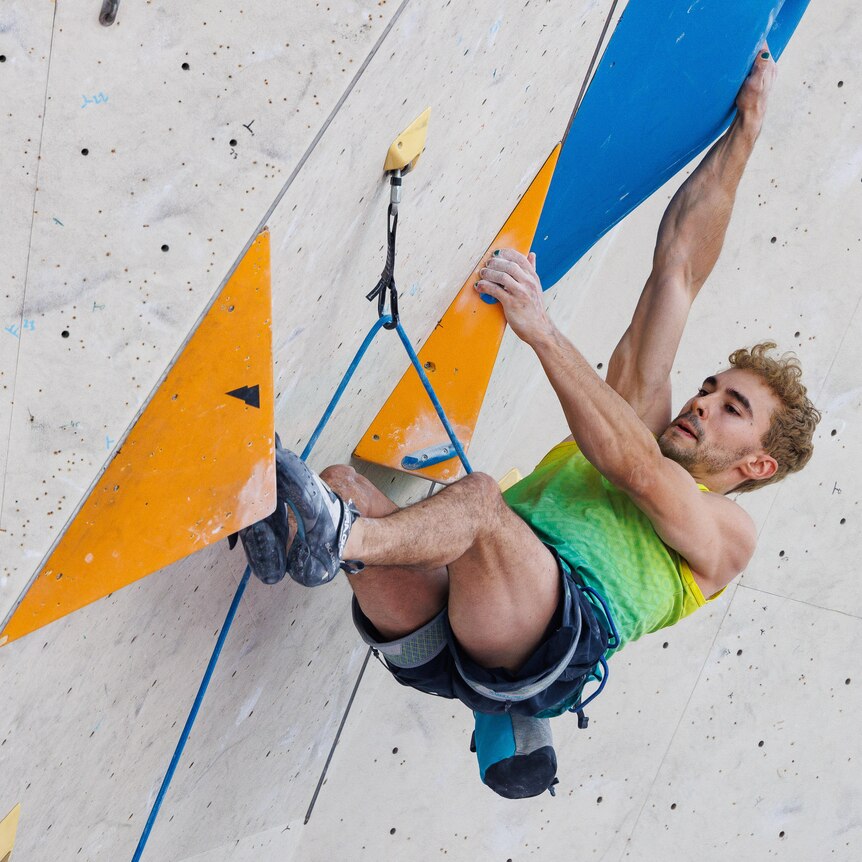 Sport climber Campbell Harrison has his legs and arms outstretched on boulders while scaling an indoor rock climbing wall.