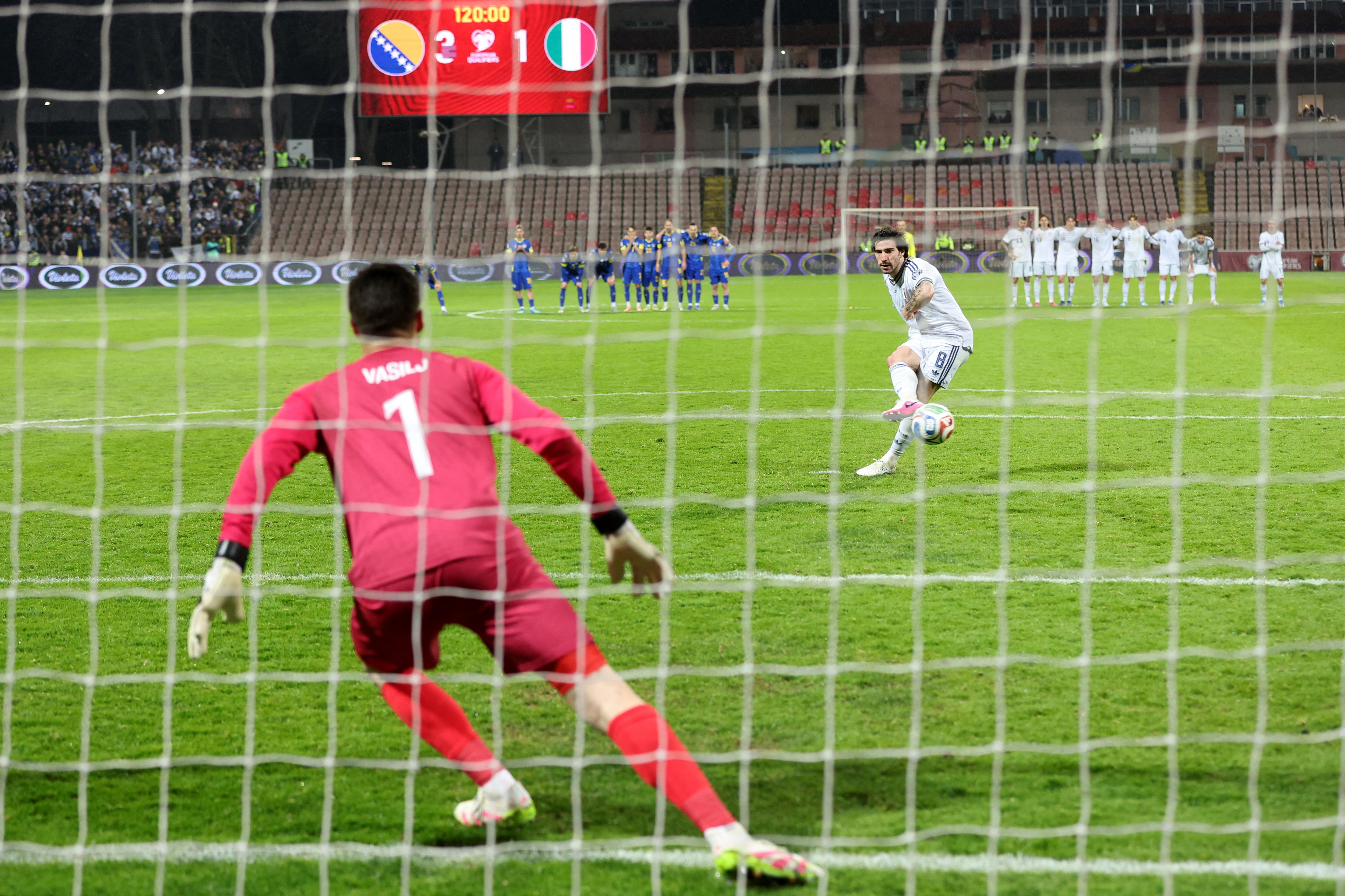An Italian player makes a shot on goal as a Bosnian goalkeeper crouches in wait.