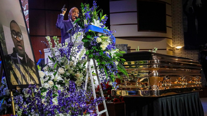 Reverend Al Sharpton lifts his hand as he delivers a eulogy at George Floyd's memorial in front of a casket and portrait
