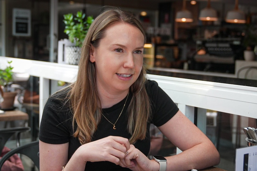 A woman in her early thirties sits at a cafe table and looks to her left talking