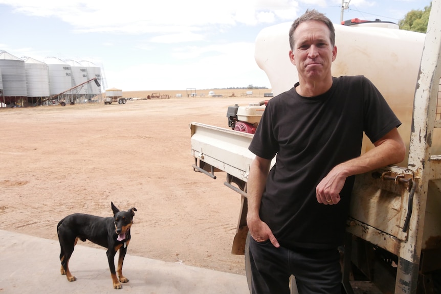 a man leans on a ute next to a dog