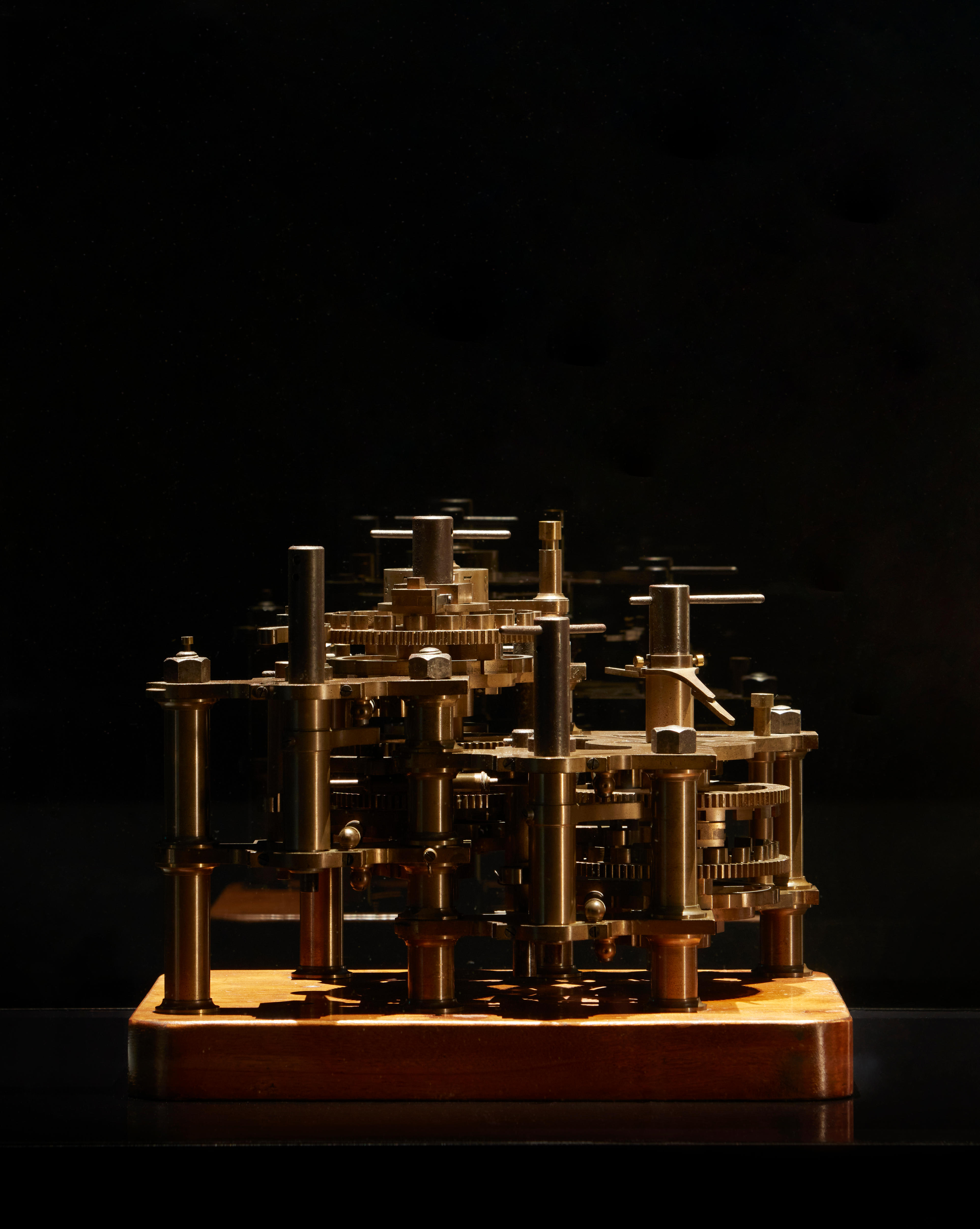 A 19-century calculating engine made from bronze, steel and wood, sitting in a display cabinet.